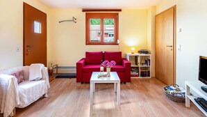 A living room with a red sofa, a white coffee table, a TV stand, and a bookshelf. - Holiday Apartment "Hach" with Private Terrace & Wi-Fi (Sulzburg)