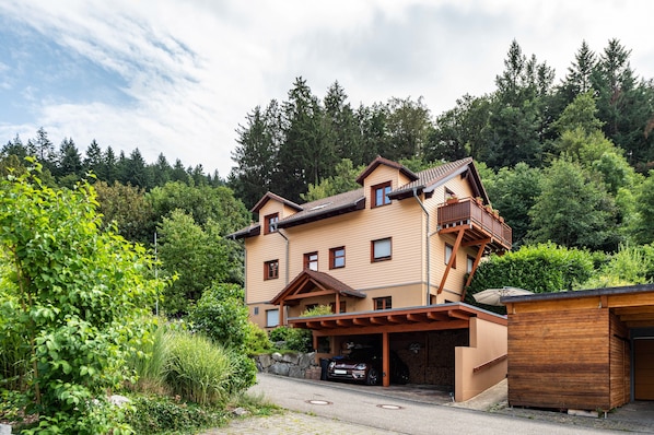A two-story house with a garage, surrounded by greenery and trees.