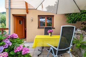 An outdoor patio with a table and chair, a door, and a window with a view of the sky.