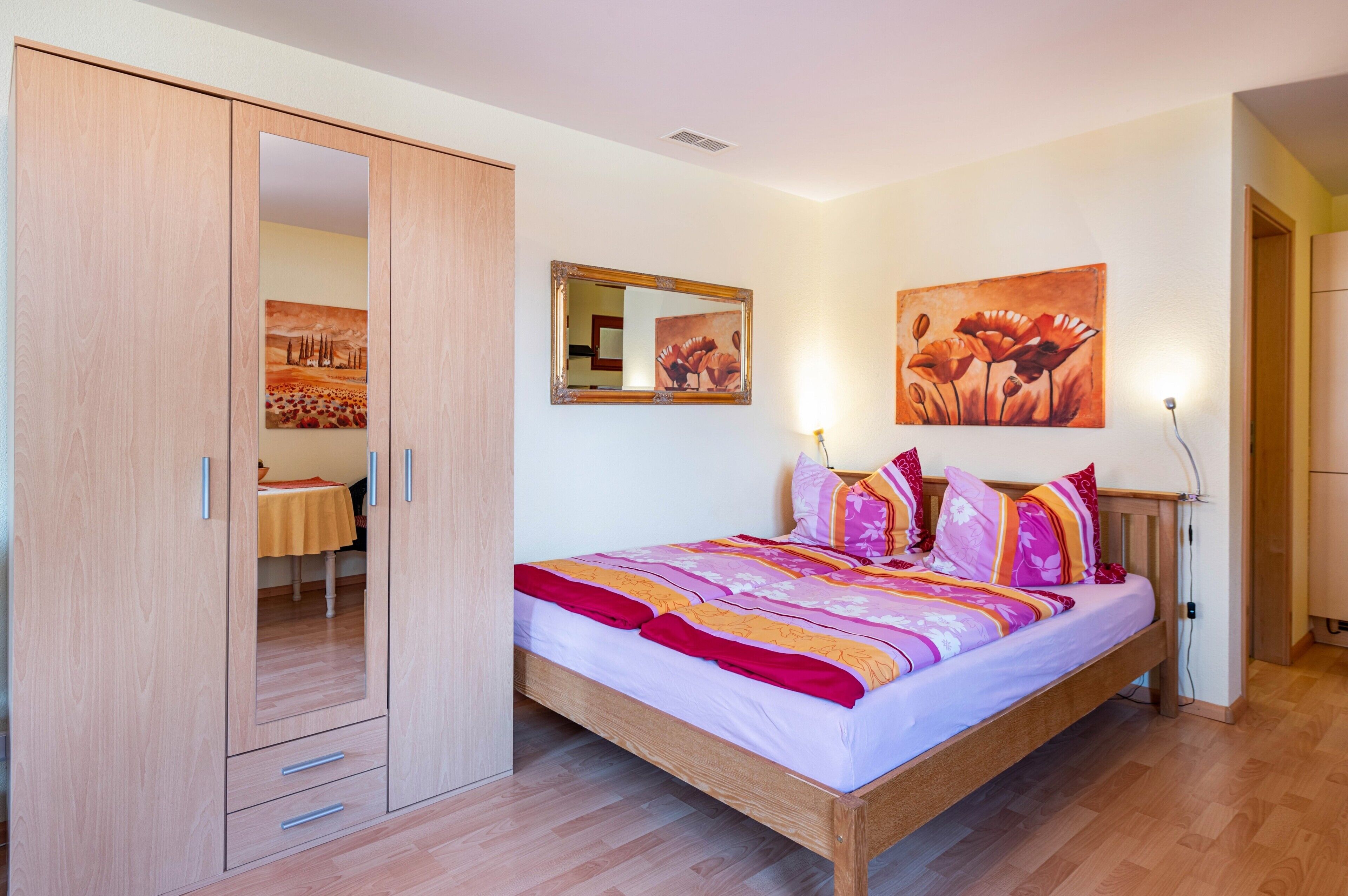 Un dormitorio con una cama de madera, un armario, un espejo y dos cuadros en la pared.