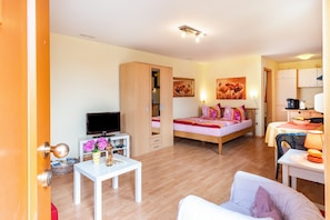A compact living space with a bed, a television, a dining area, and a kitchenette.