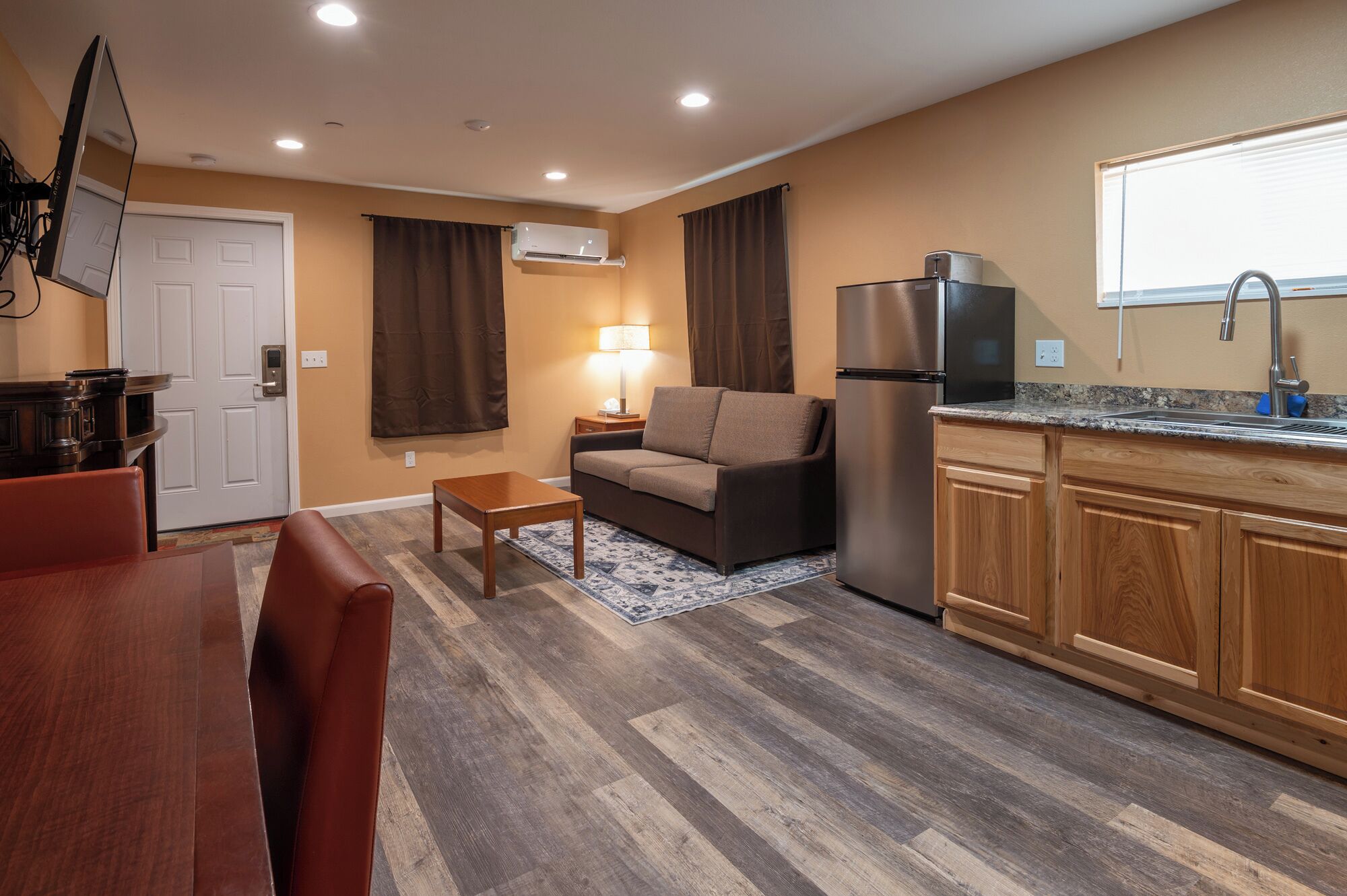 A compact living space with a kitchenette, a sofa, a small table, and a TV mounted on the wall.