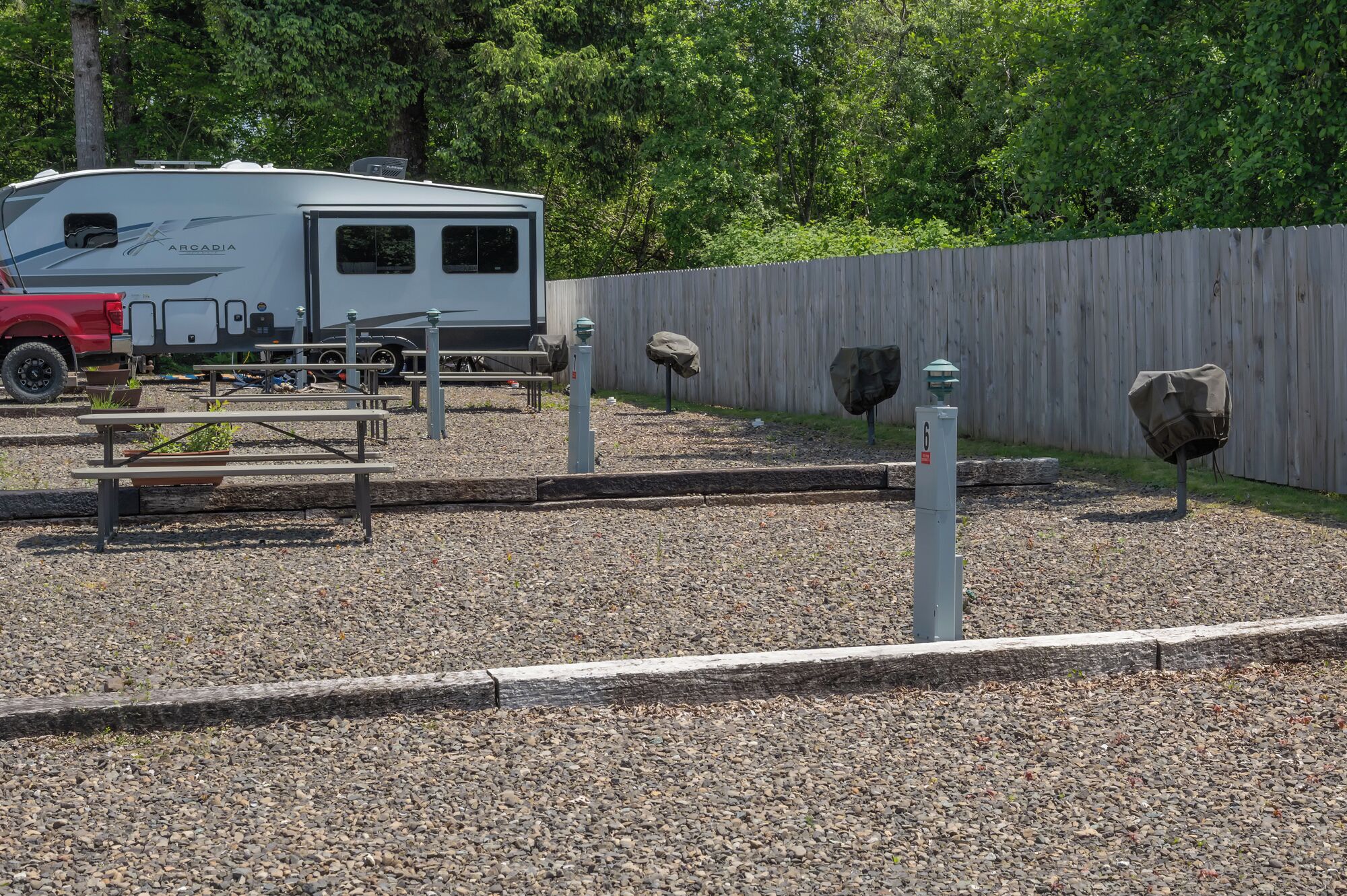 En campingplads med picnicborde, en overdækket autocamper og et træhegn.