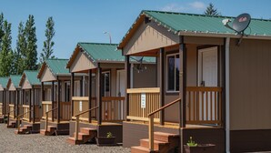 A row of small, single-story cabins with wooden railings and steps leading to the door. Each cabin has a small porch and a satellite dish. - Far West RV Park and Cabins (Forks)