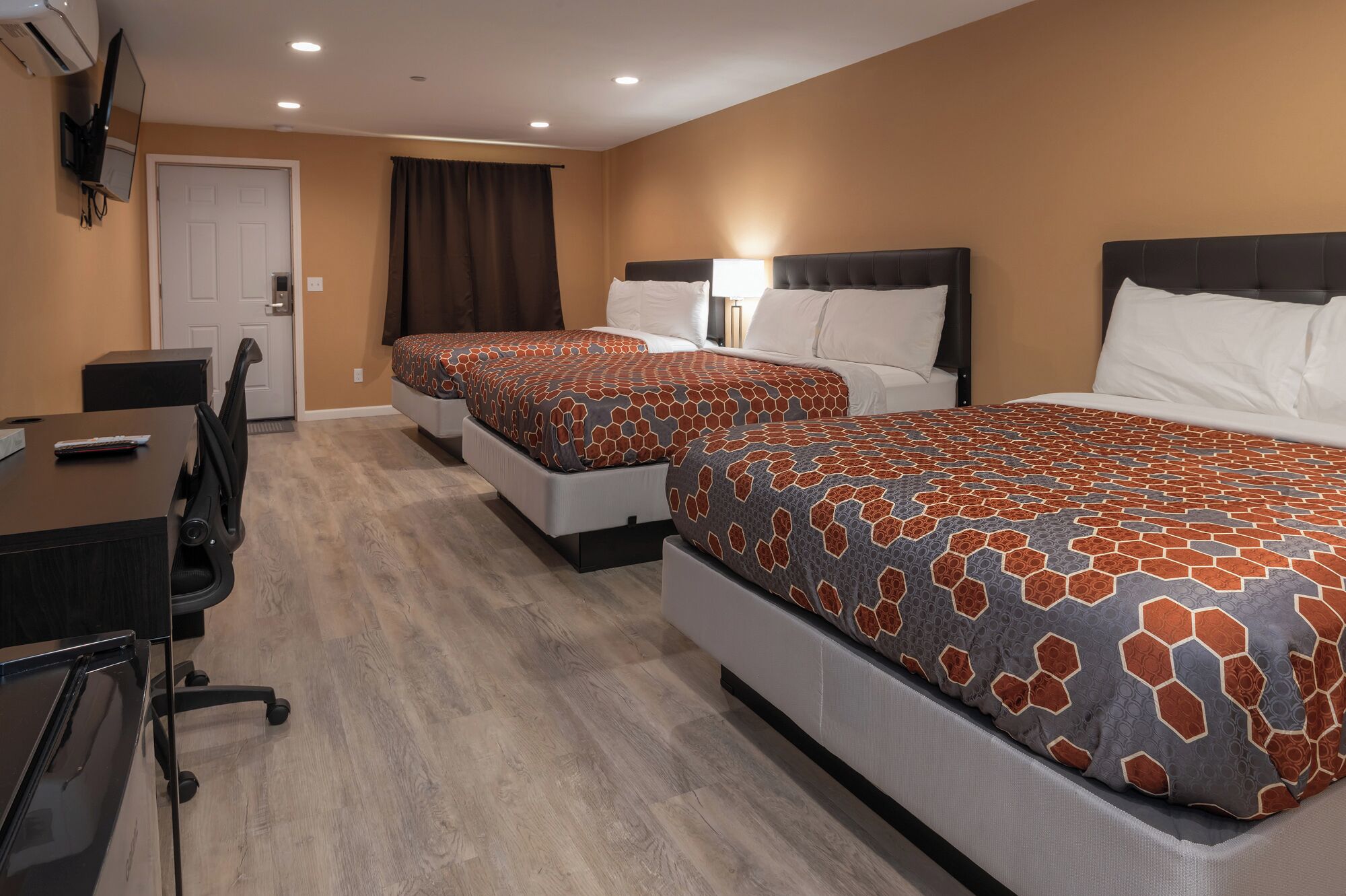 A hotel room with two beds, a desk, a chair, and a TV mounted on the wall.