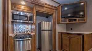 A compact kitchen with a gas stove, stainless steel refrigerator, and a microwave. - Far West RV Park and Cabins (Forks)