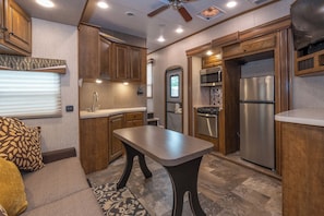 A compact kitchen with wooden cabinets, a stainless steel refrigerator, a microwave, and a stove. - Far West RV Park and Cabins (Forks)
