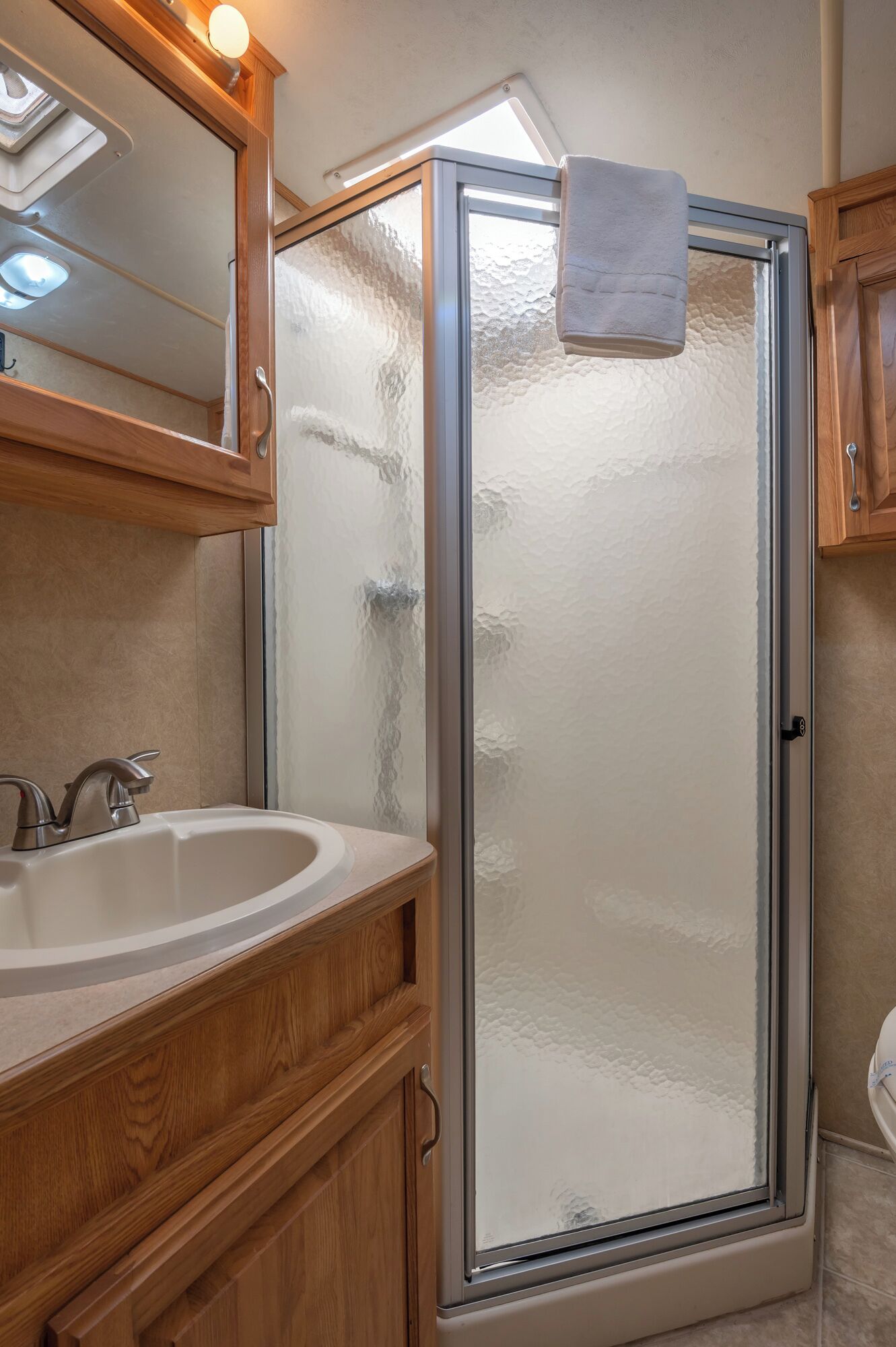 A bathroom with a glass shower enclosure, wooden vanity, and a mirror above the sink.