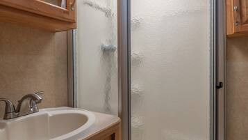 A bathroom with a glass shower enclosure, wooden vanity, and a mirror above the sink.