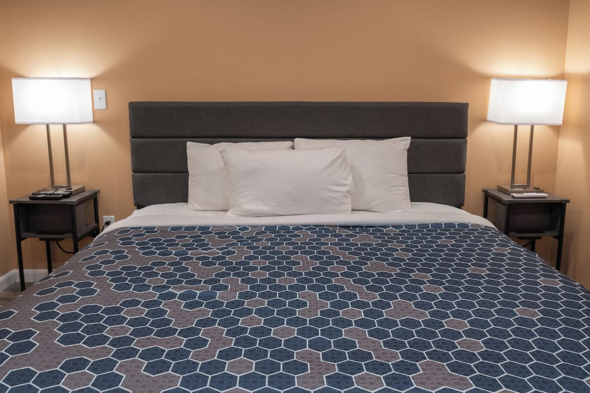 A hotel room with a bed, two bedside lamps, and a patterned bedspread.