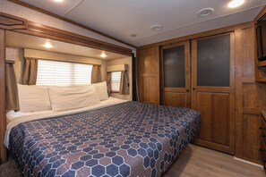 A bedroom with a bed, wooden wardrobe, and a window with curtains. - Far West RV Park and Cabins (Forks)