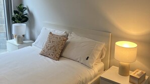 A neatly made bed with white linens, a floral pillow, and a bedside lamp on a nightstand.