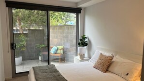 A bedroom with a bed, a sliding glass door leading to an outdoor area with a bench and plants.