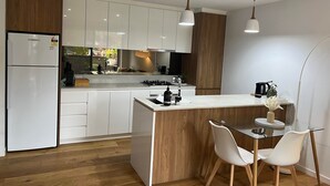 A modern kitchen with white cabinets, a central island with a glass top, and two pendant lights.