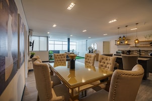 Uma sala de jantar moderna com mesa de vidro, cadeiras estofadas e iluminação pendente.