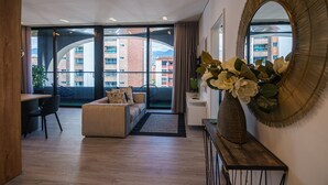 A modern living room with a sofa, dining table, and chairs, large windows with a view of buildings, and a decorative vase with flowers. - First Class Hotel (Medellín)