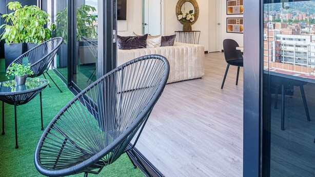 A modern interior with a balcony, green artificial grass, and a view of the city. - First Class Hotel (Medellín)