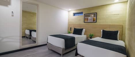 A hotel room with two beds, a large mirror, a wooden headboard, and a small shelf with a picture frame.