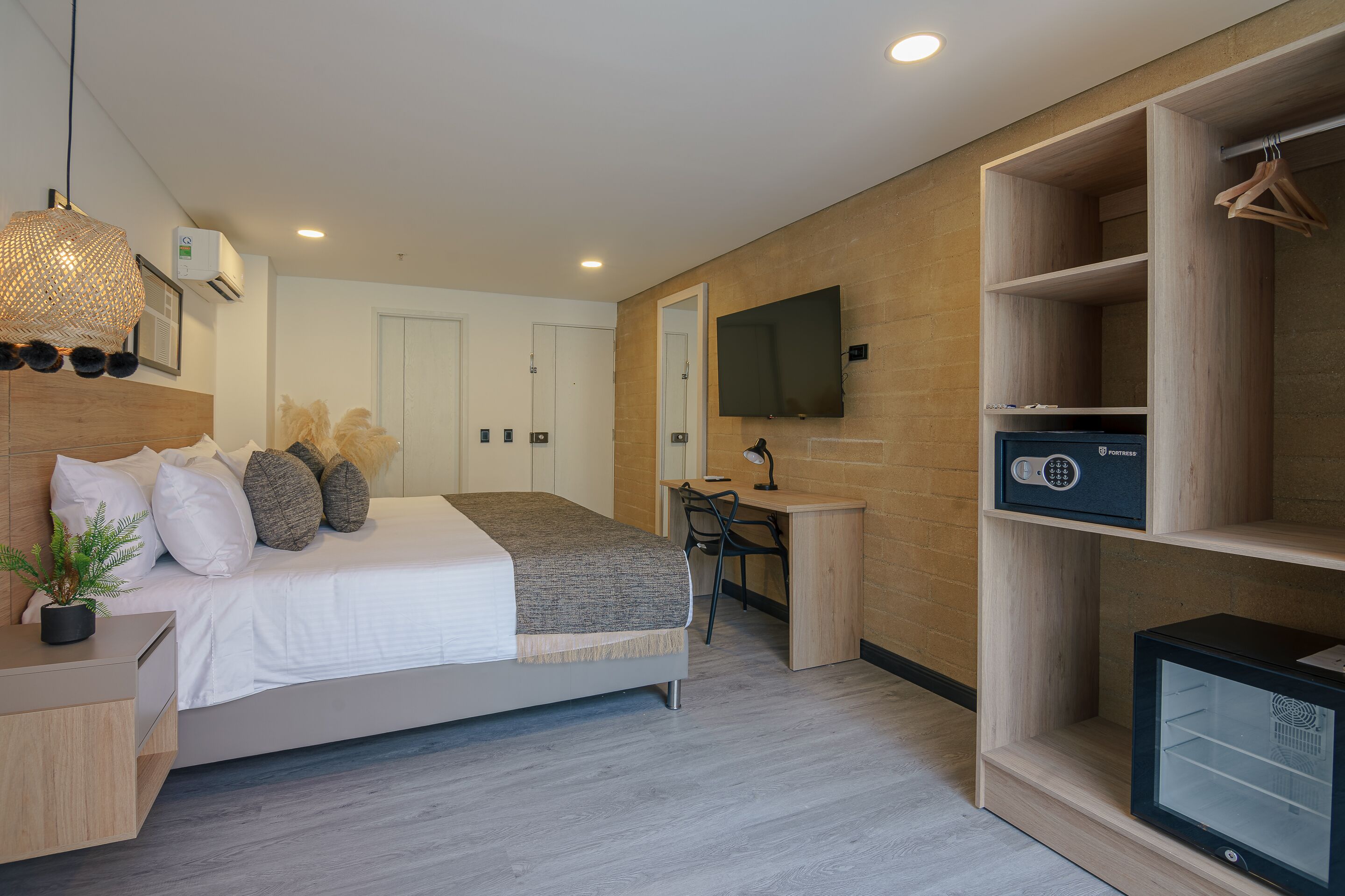 A modern bedroom with a bed, bedside table, dresser, desk, chair, TV, wardrobe, and a potted plant.