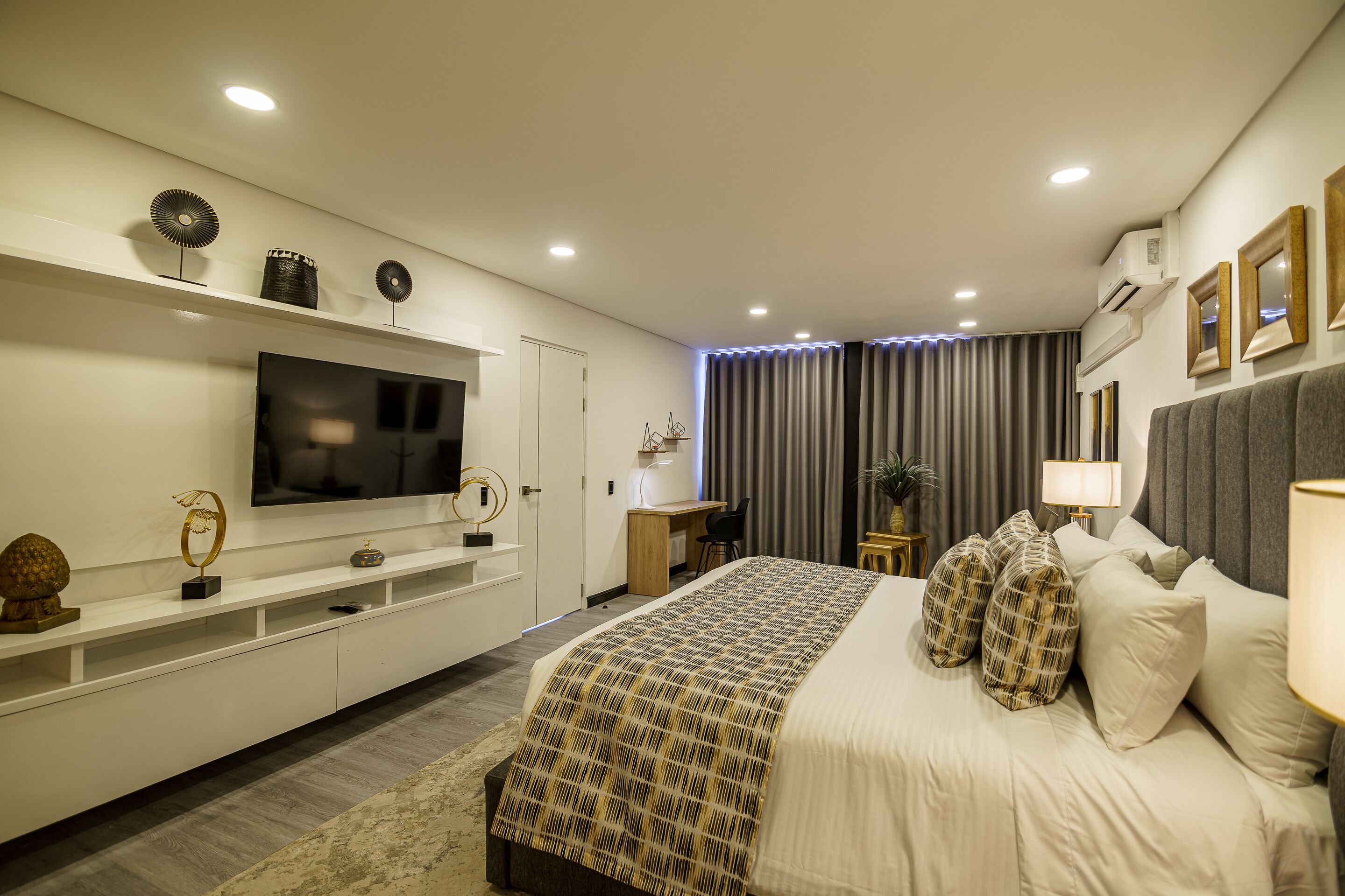 A modern hotel bedroom with a large bed, a flat-screen TV, a desk, and a seating area.