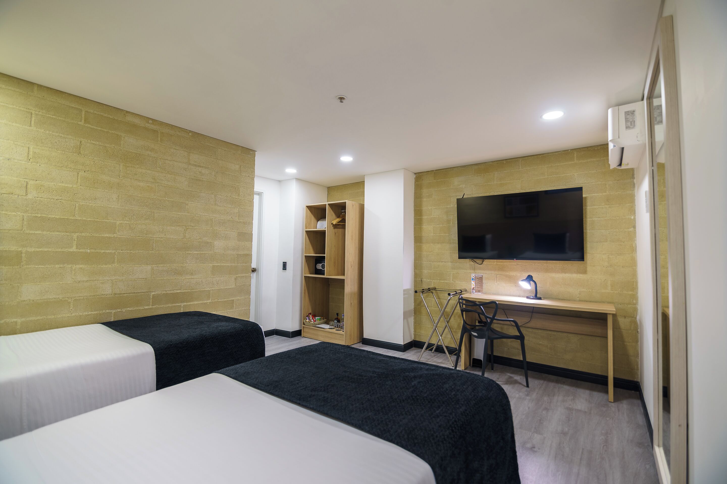 A hotel room with two beds, a desk with a chair, a television, and a wardrobe.