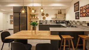 A modern kitchen with a central island, black chairs, a wooden table, hanging pendant lights, and a tiled backsplash. - First Class Hotel (Medellín)