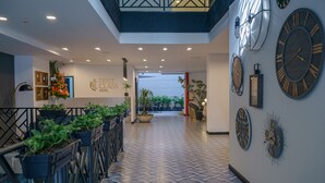 A hotel lobby with a reception desk, potted plants, and large wall clocks. - First Class Hotel (Medellín)