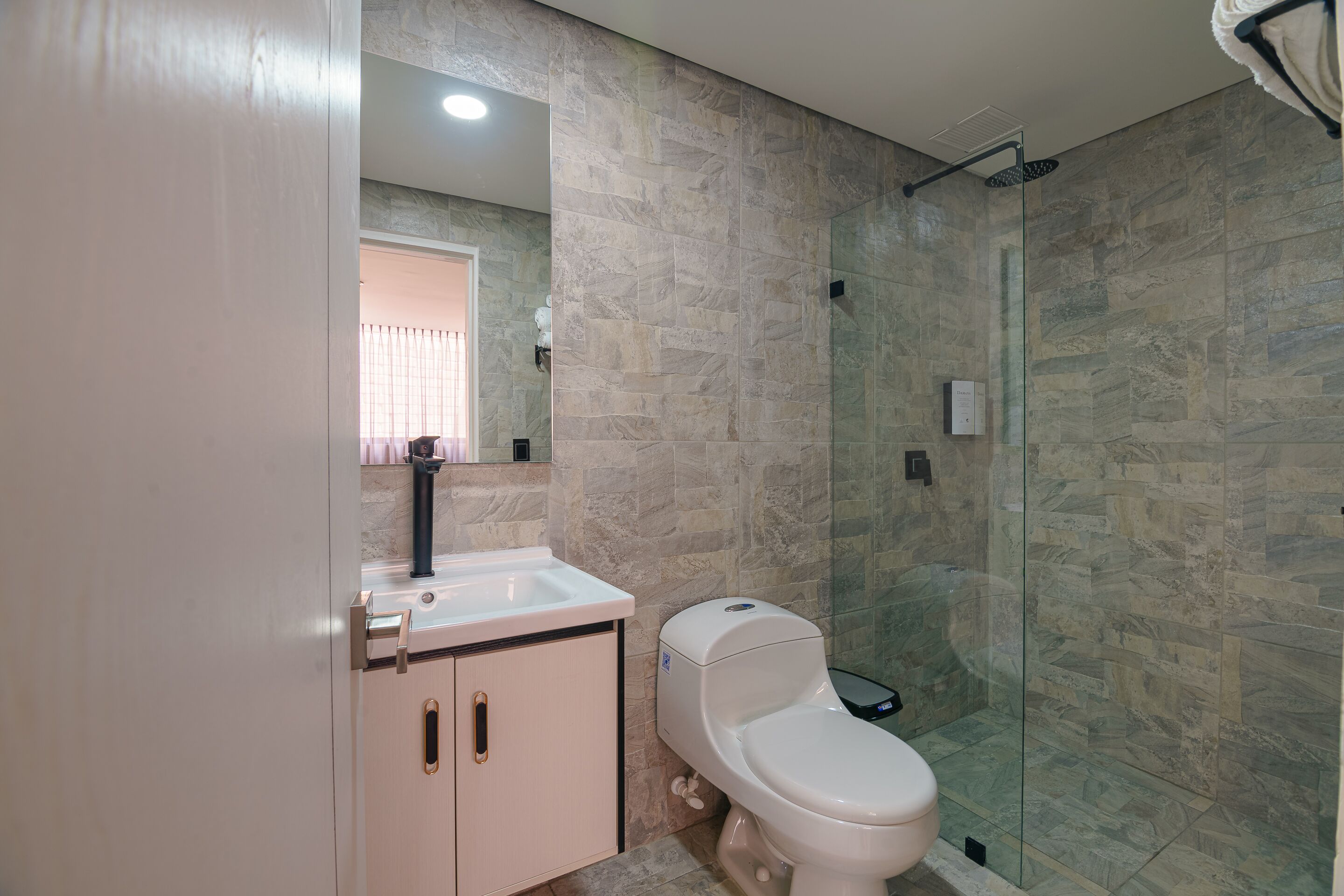 A modern bathroom with a glass shower enclosure, a white toilet, and a beige vanity with a mirror.