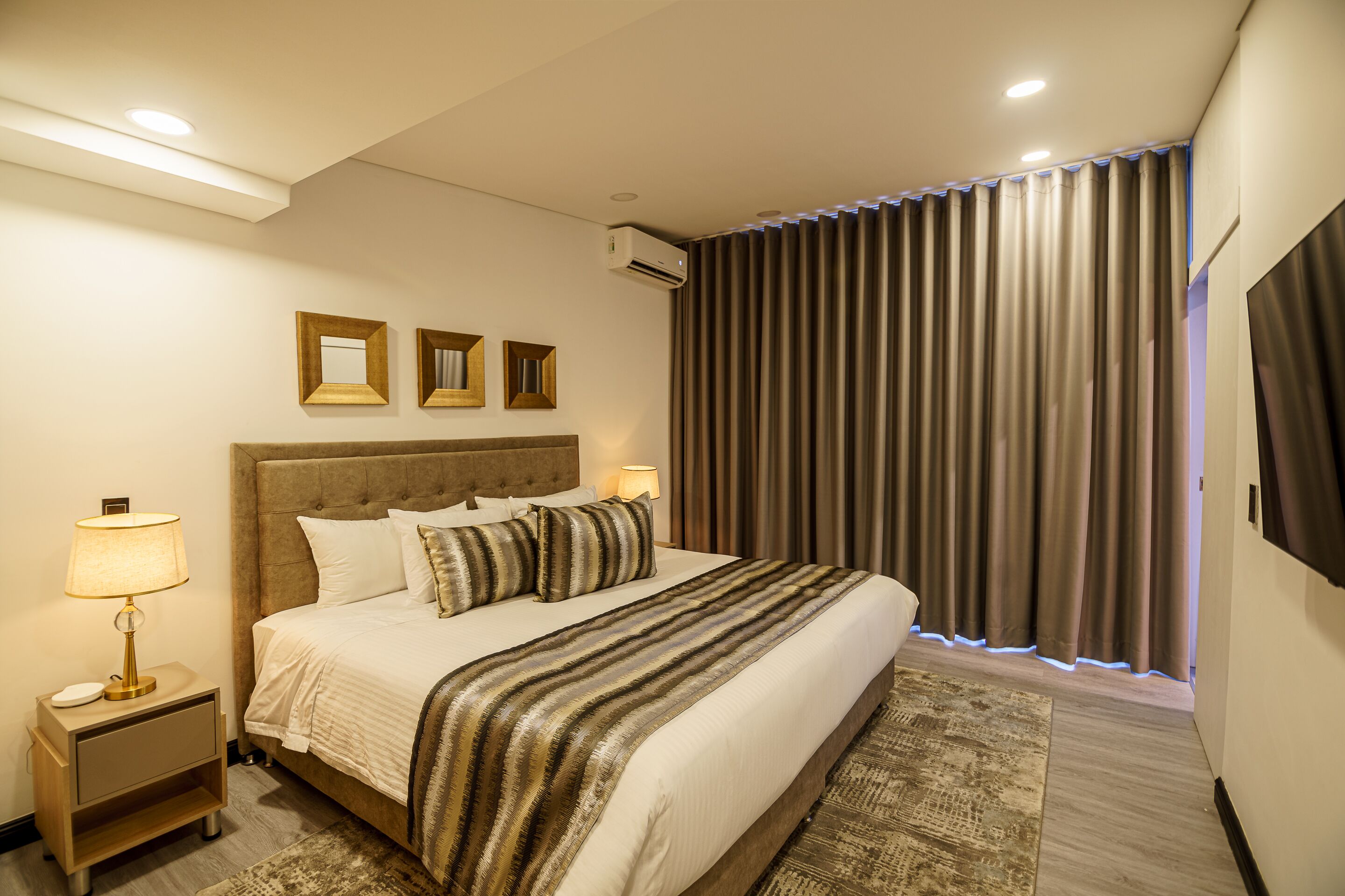 A hotel room with a large bed, a nightstand with a lamp, and a wall-mounted TV.