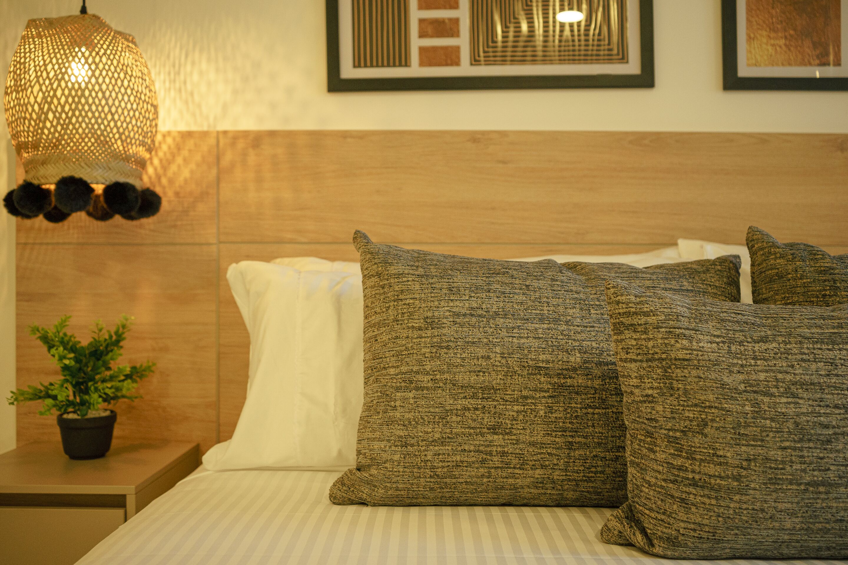 A neatly made bed with striped bedding, a textured pillow, and a hanging light fixture.