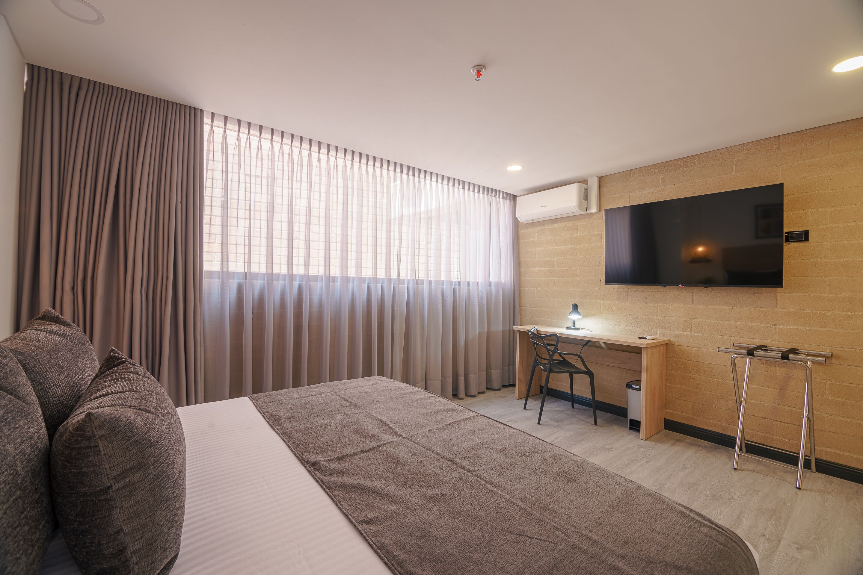 A hotel room with a bed, a desk, a chair, a TV, and a window with curtains.