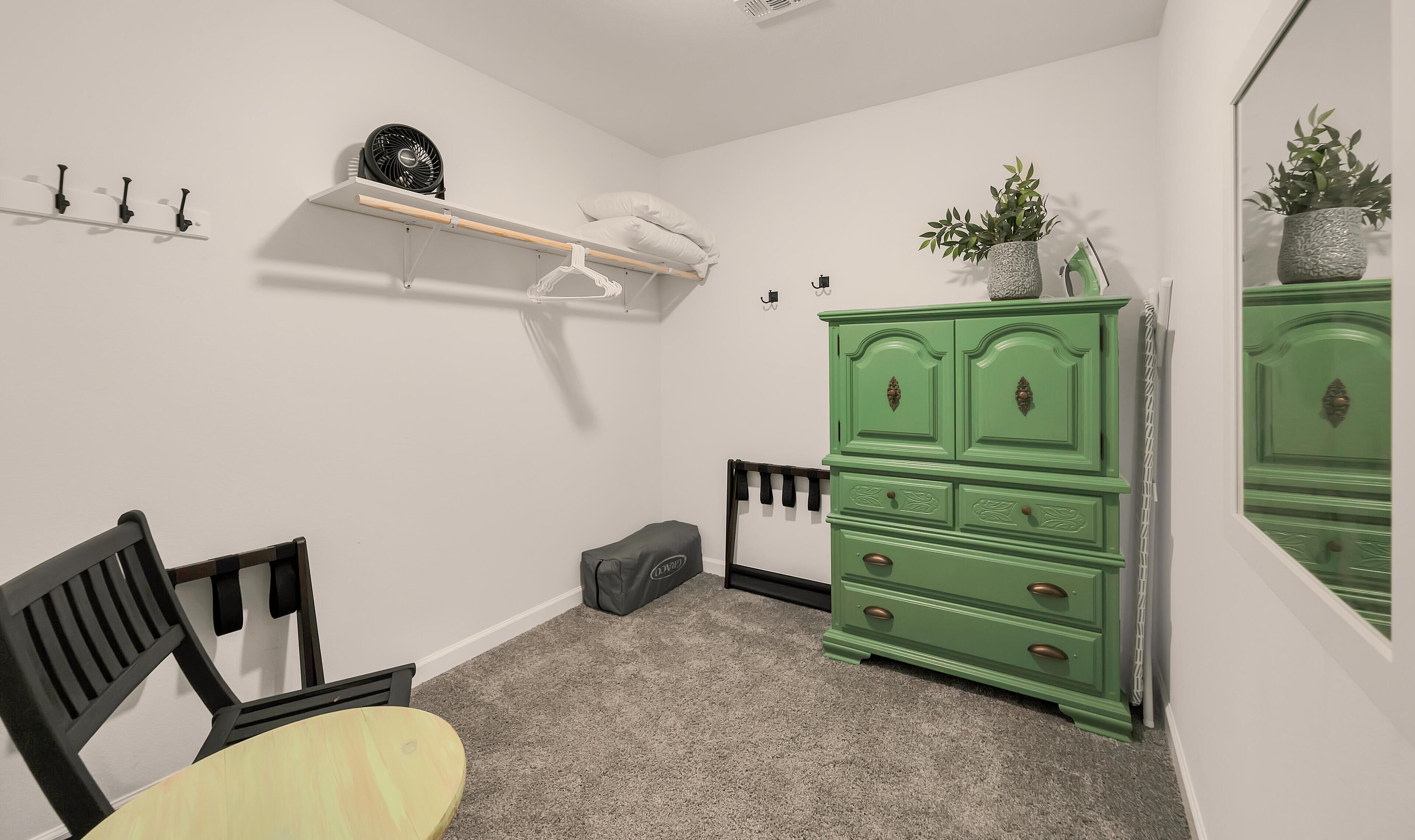 A room with a green dresser, a small table, and a chair. There is a shelf with a fan and a plant.