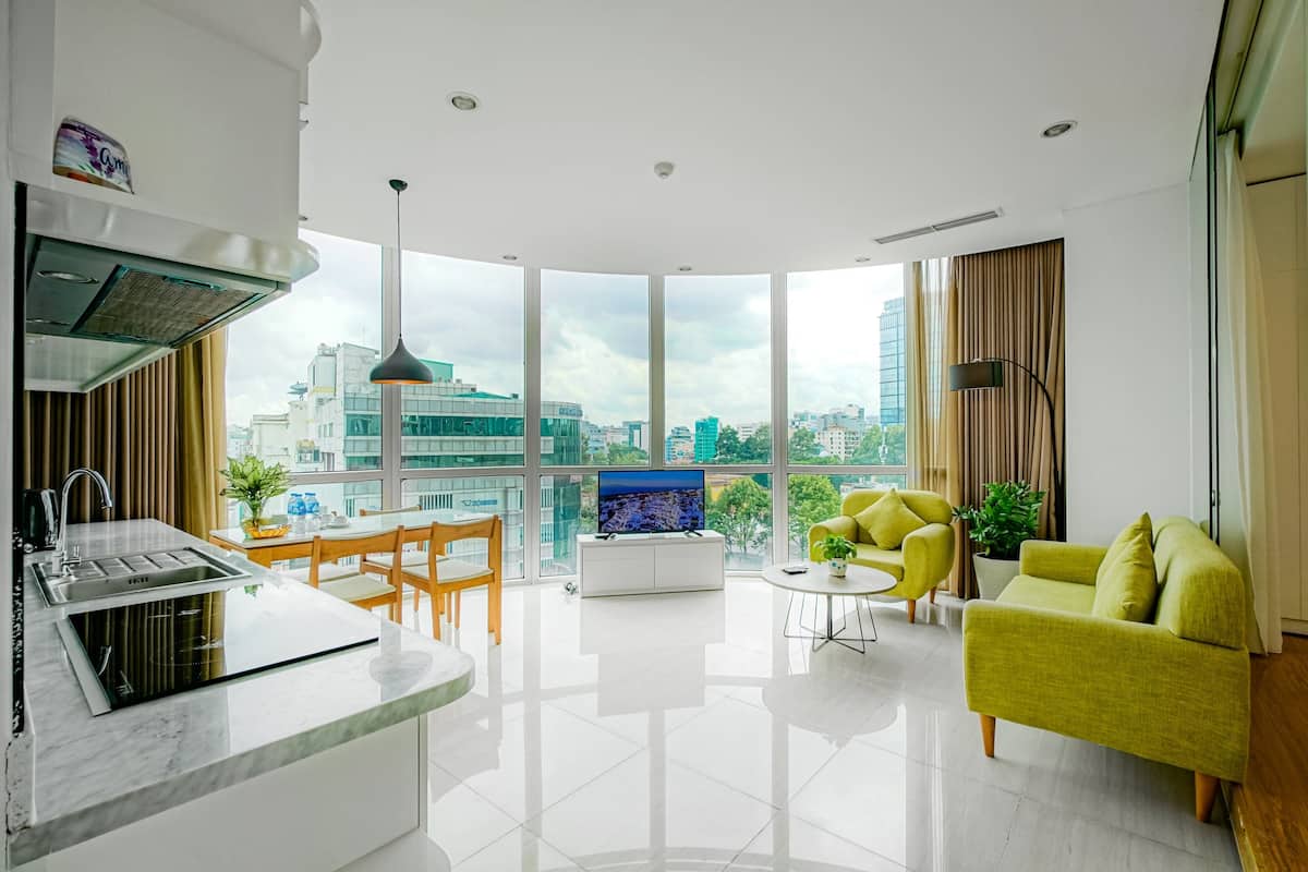 A modern living room with a kitchen area, large windows, and a city view.