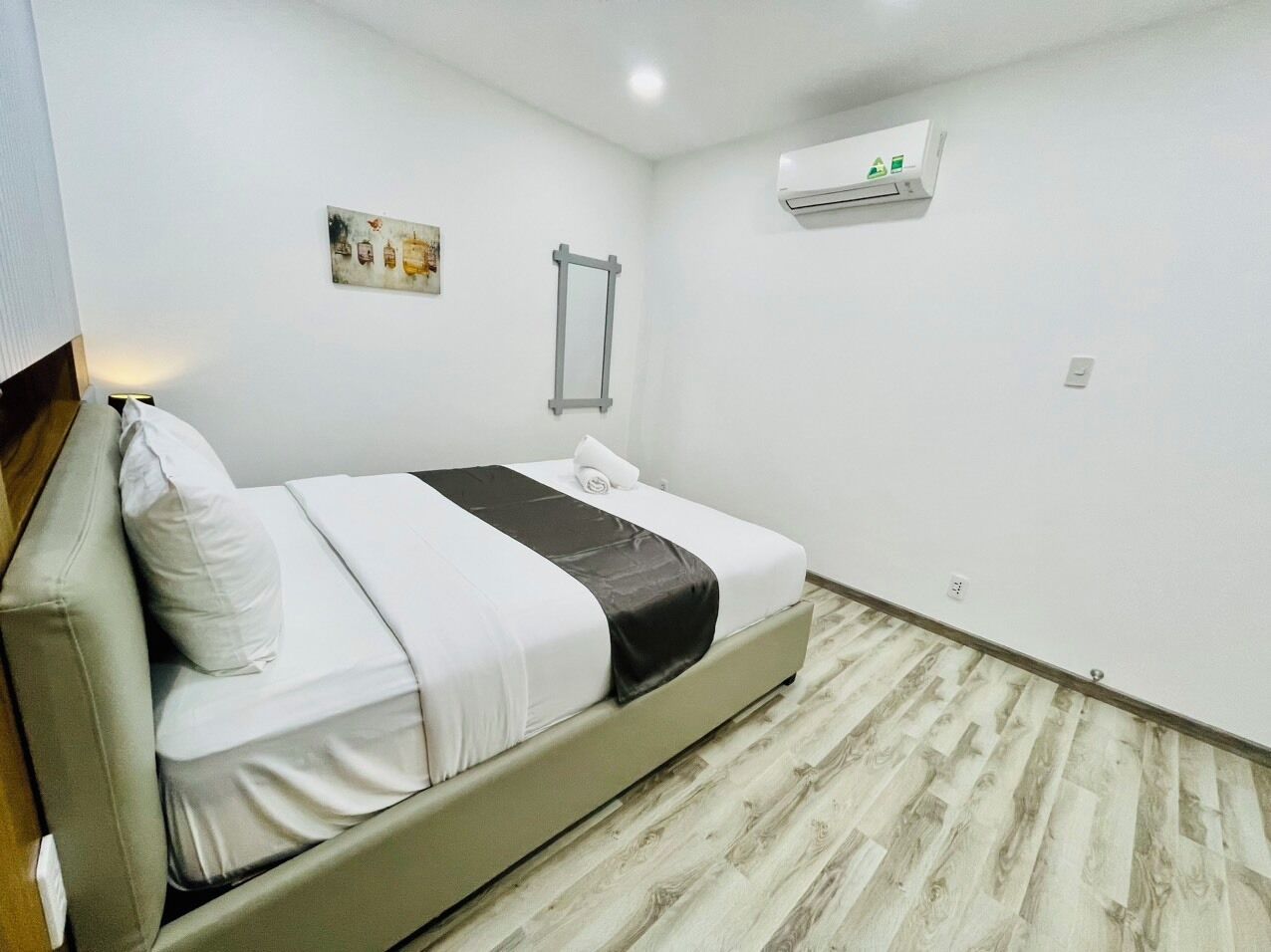 A bedroom with a bed, a wall-mounted air conditioner, and a wooden floor.