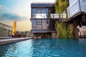 A modern building with a rooftop pool, glass railings, and outdoor seating.