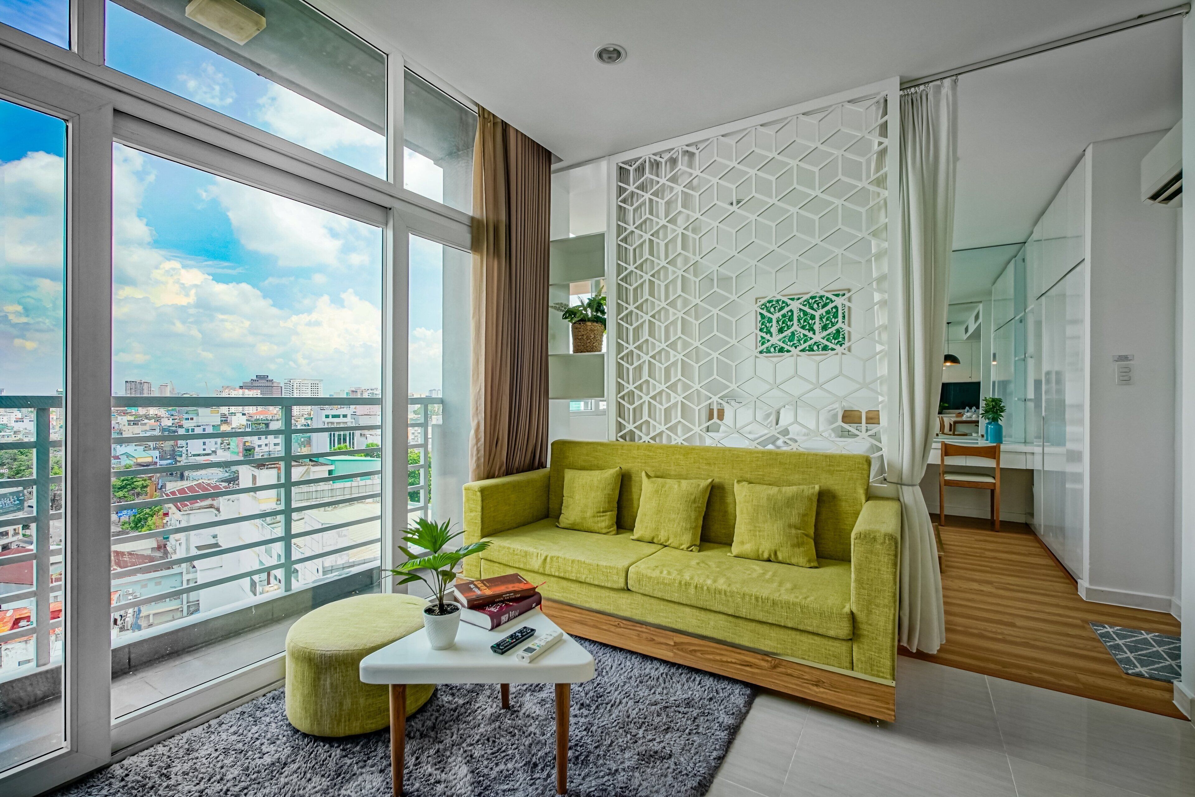 A modern living room with a green sofa, a white coffee table, and a view of the city through large windows.