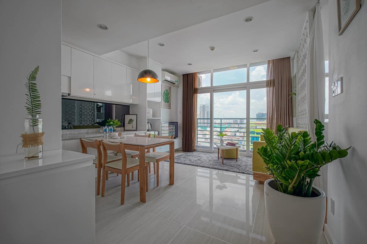 A modern kitchen with white cabinets, a dining area with wooden chairs, and a large window with a view of the city.