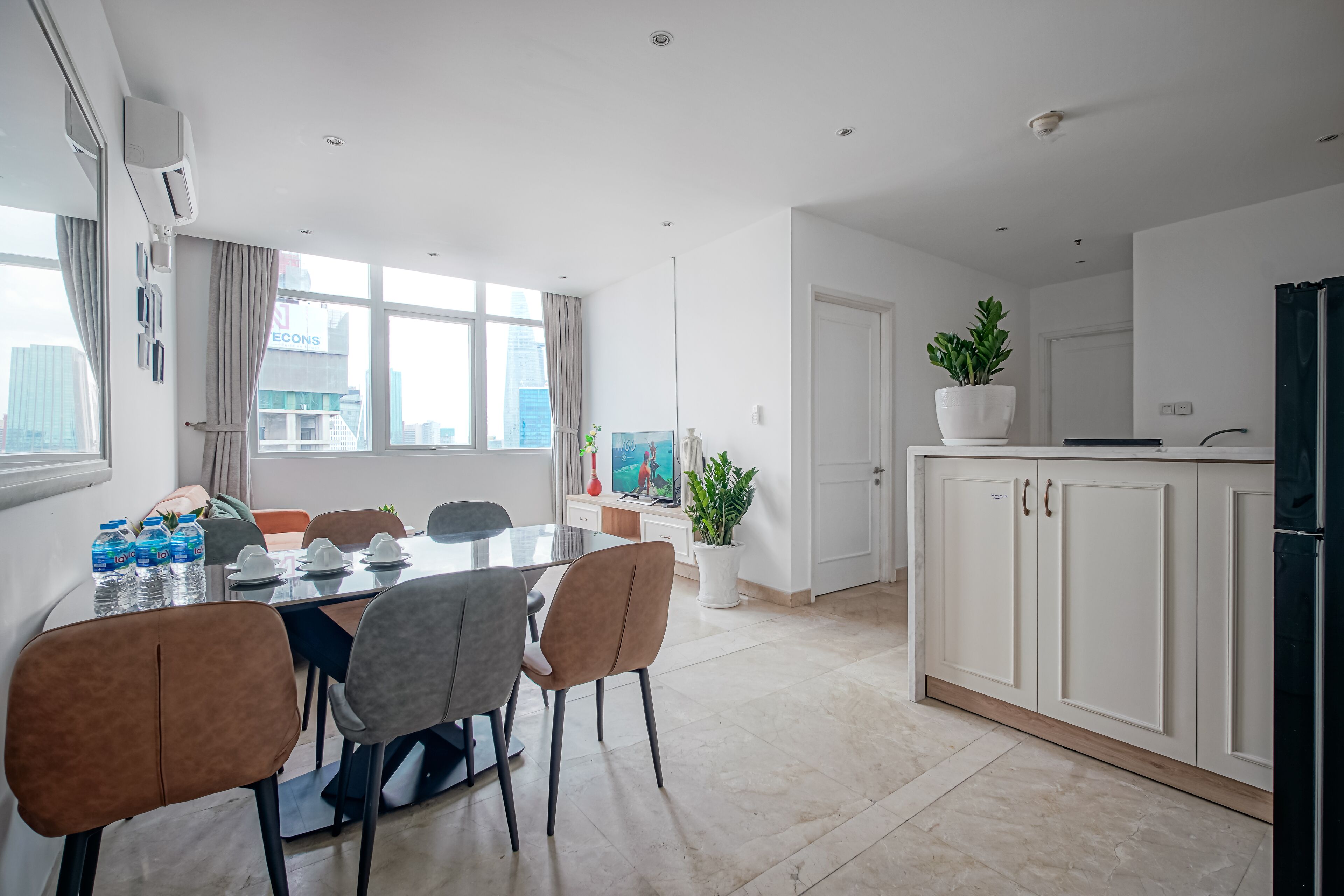 Una cocina moderna con armarios blancos, un comedor con mesa de vidrio y vistas a la ciudad a través de amplios ventanales.