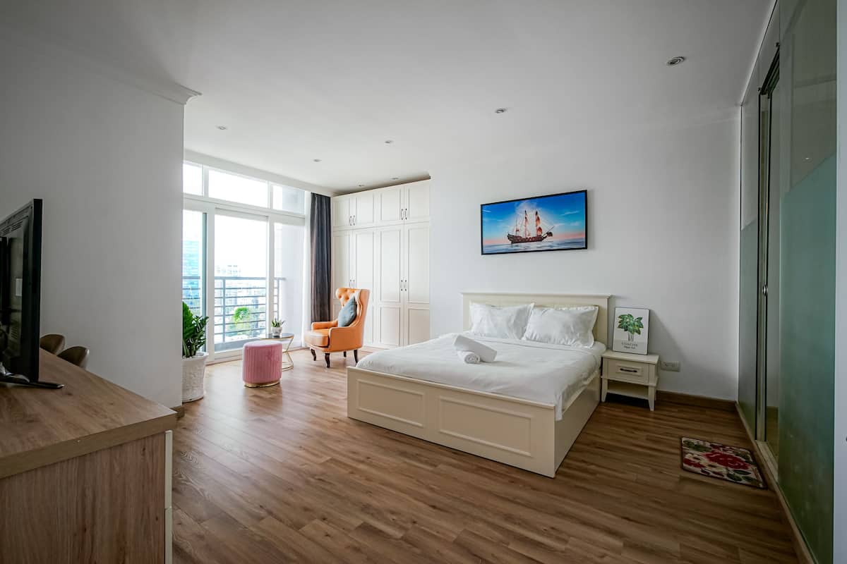 A bedroom with a bed, a TV, a desk, a chair, a wardrobe, and a window with a city view.