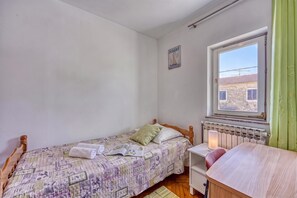 Quarto pequeno com cama de solteiro, janela, radiador e vista para o exterior.