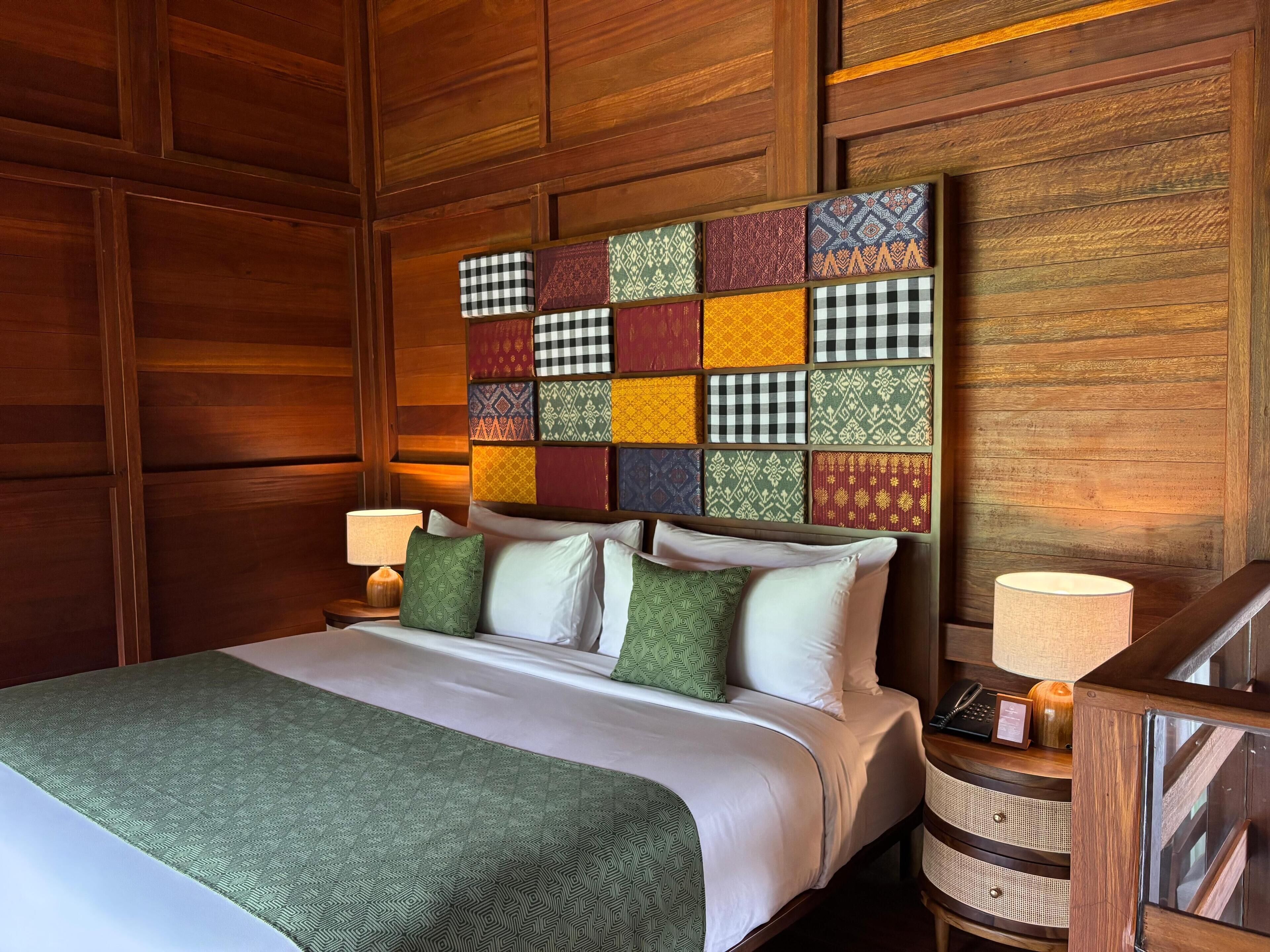 A neatly made bed with a patterned headboard, a bedside table with a lamp, and a wooden nightstand.
