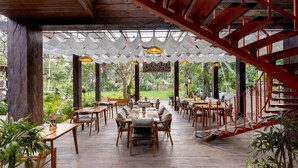 An outdoor dining area with wooden tables and chairs, surrounded by plants and a red staircase. - AnandaDara Ubud Resort & Spa (Ubud)
