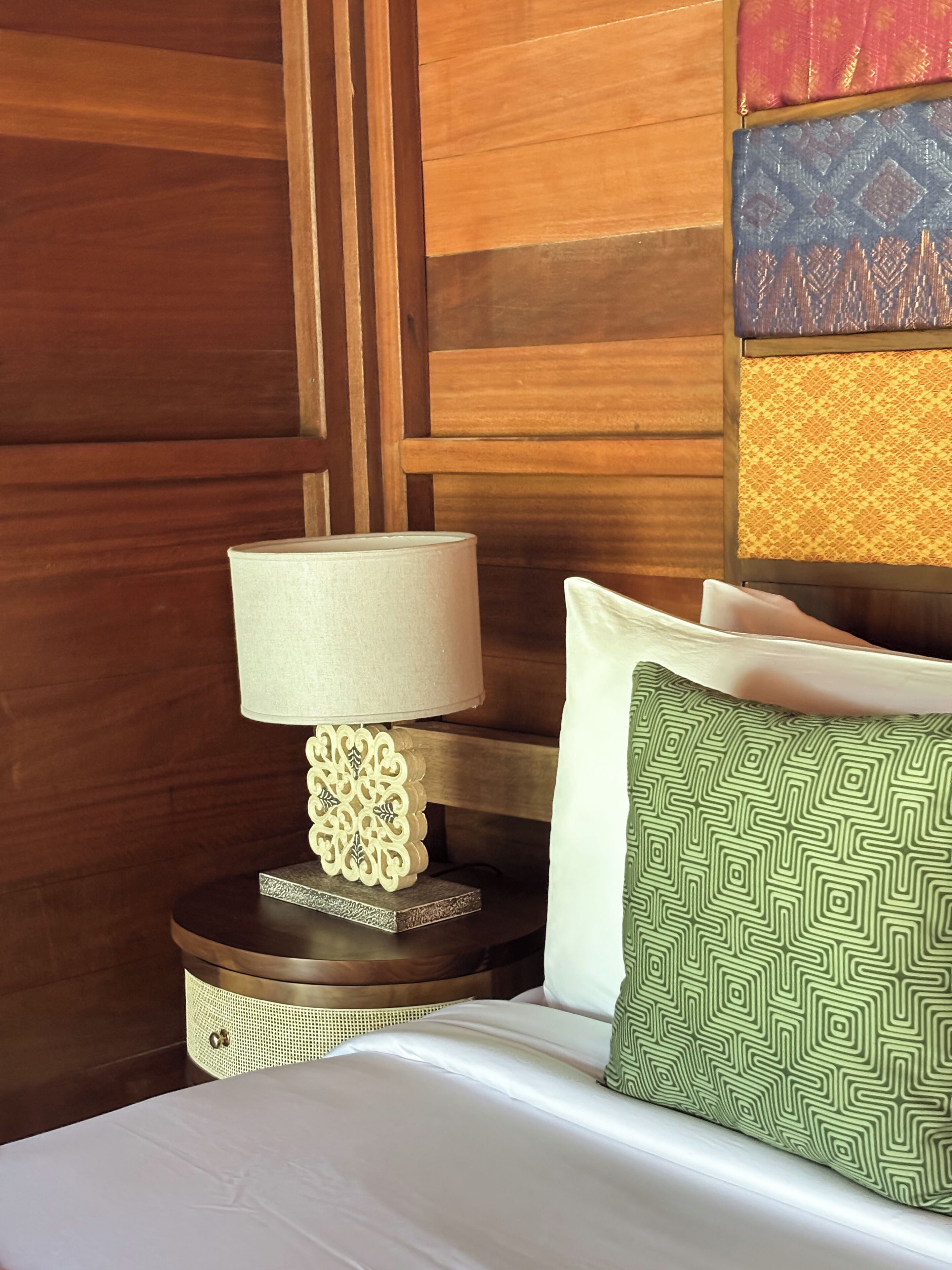 A neatly made bed with white linens, a decorative bedside lamp, and a patterned pillow.
