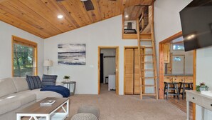 A spacious living area with a high ceiling, wooden beams, a sofa, a coffee table, ottomans, a painting, and a TV. - Adalee - Table Rock Lake, Roaring River, Eureka Springs, Dogwood Canyon (Eagle Rock)
