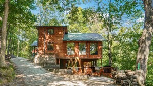 A rustic cabin with a stone foundation, a wooden deck, and a metal roof, surrounded by dense forest. - Adalee - Table Rock Lake, Roaring River, Eureka Springs, Dogwood Canyon (Eagle Rock)