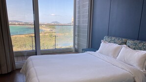 Un dormitorio con una cama grande, vistas a un paisaje costero y una pared azul.