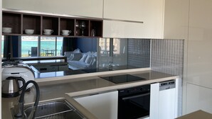 Una cocina moderna con horno empotrado, lavavajillas y vistas a un balcón con sofá blanco y mesa.