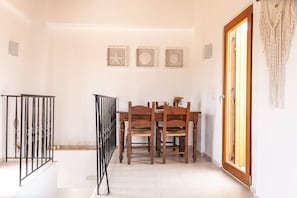 A dining area with a wooden table and chairs, a staircase with a railing, and a door with a macrame curtain. - Bental's Dream Place With Lake And Sea View (Kavallos)