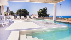 Un espace piscine avec des chaises longues, un coin salon abrité et une vue sur la mer.