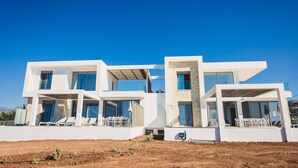 Une maison moderne à deux étages, dotée de grandes fenêtres, d’un balcon et d’un toit plat.
